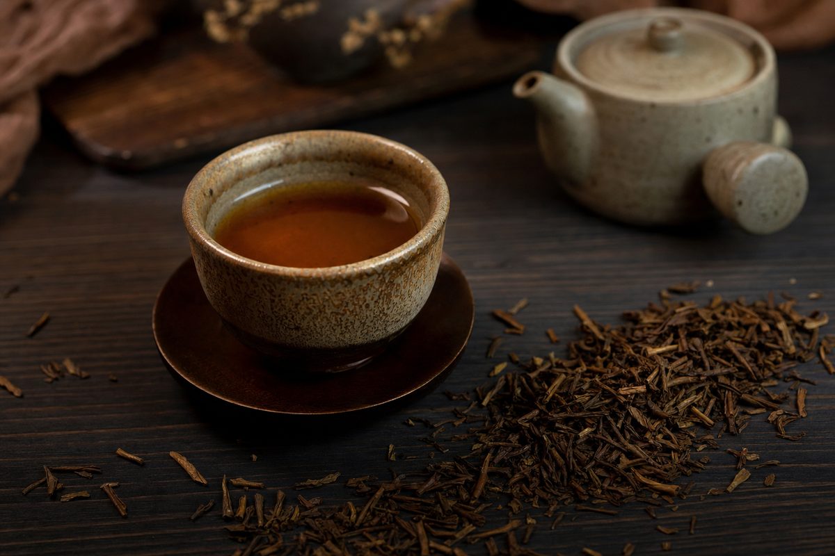 A cup of roasted hojicha with its reddish-brown color, beside scattered roasted leaves